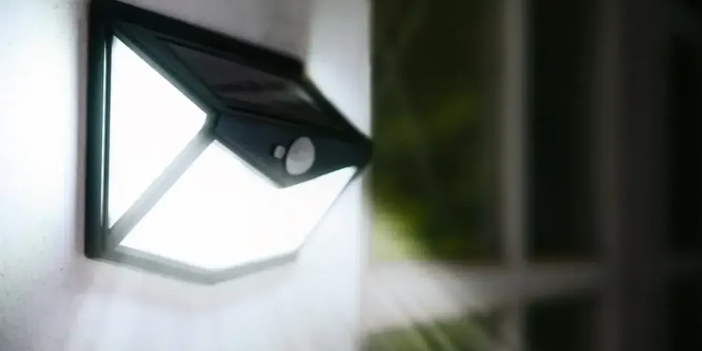 Outdoor solar-powered LED wall light glowing at night.