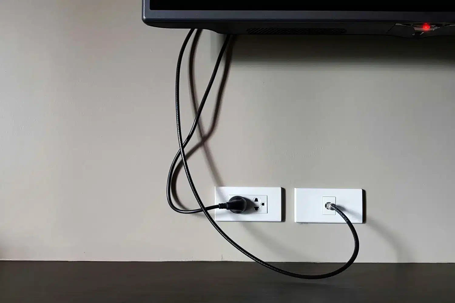 Wall-mounted TV with cables plugged into electrical and coaxial outlets.
