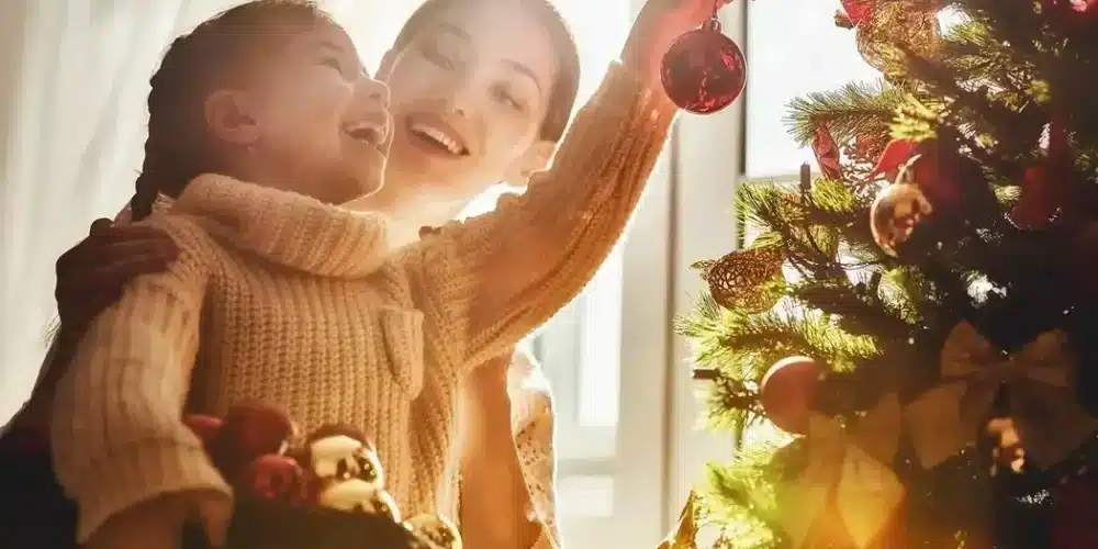 Mother and daughter joyfully decorating a Christmas tree together.