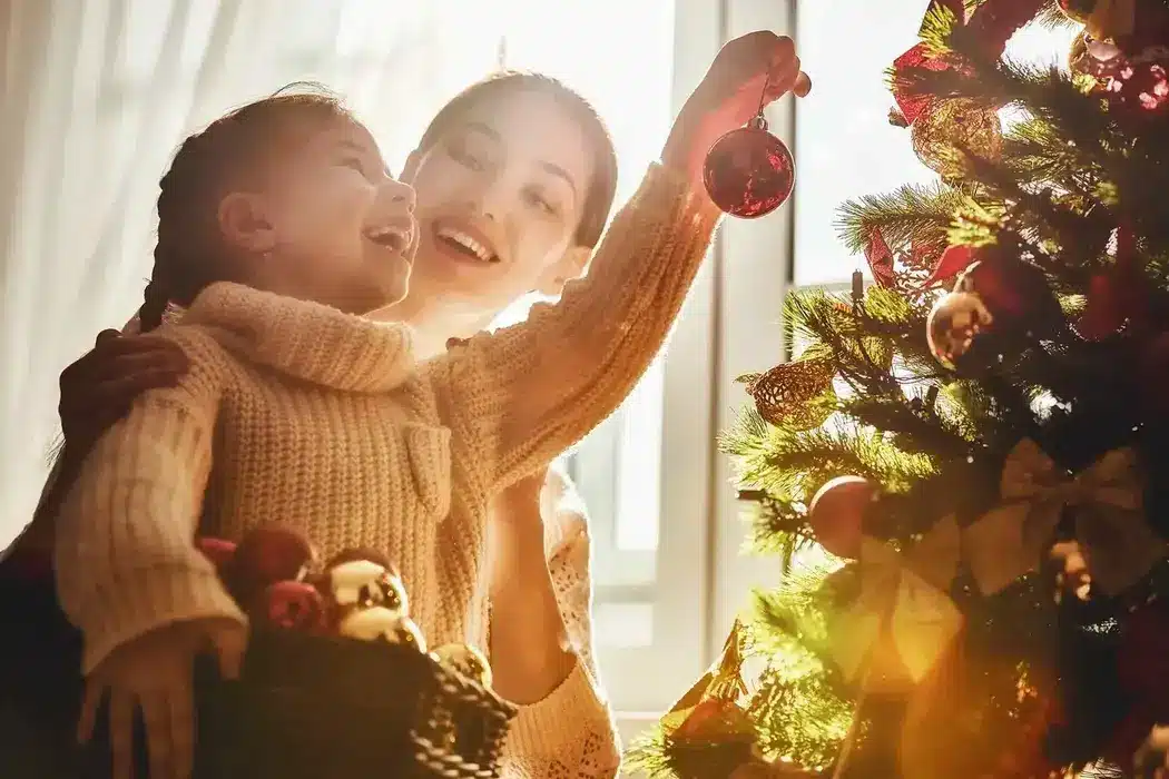 Mother and daughter joyfully decorating a Christmas tree together.