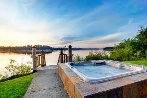 Hot tub on patio overlooking serene lakeside at sunset.