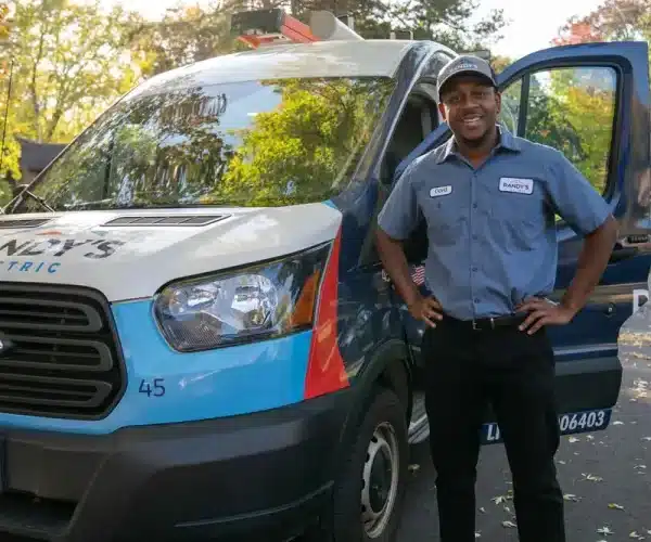Connor standing next to Randy's Electric van with open door, wearing uniform and cap.