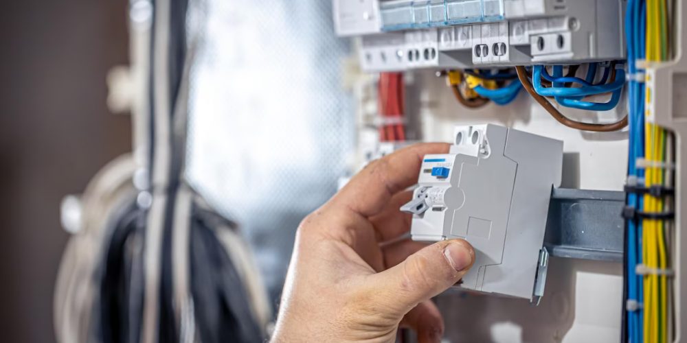 Hand replacing a circuit breaker in an electrical panel with colored wires.