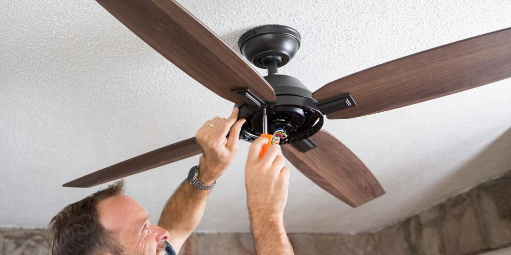 Man installing a wooden ceiling fan with a screwdriver indoors.