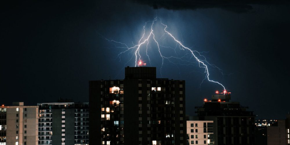 Lightning strikes over city buildings at night, illuminating the skyline.