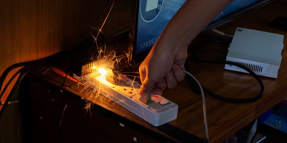 Hand pulling plug from sparking power strip, electrical safety issue.