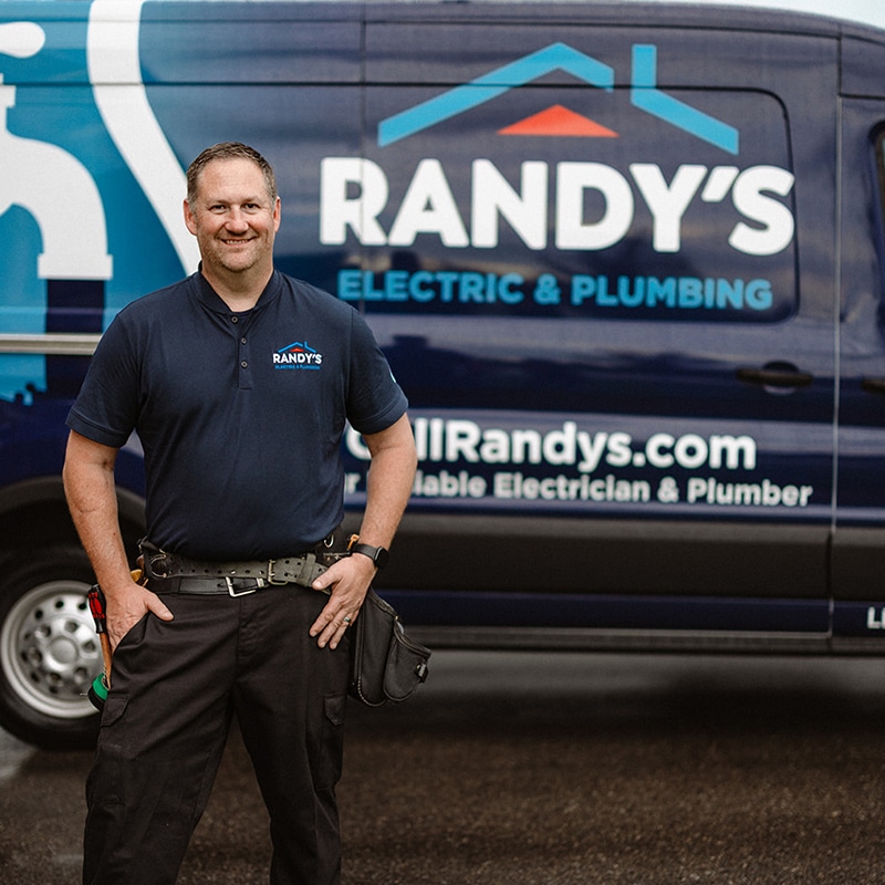 A man in front of Randy's Electric & Plumbing van, wearing a tool belt and uniform with a logo.
