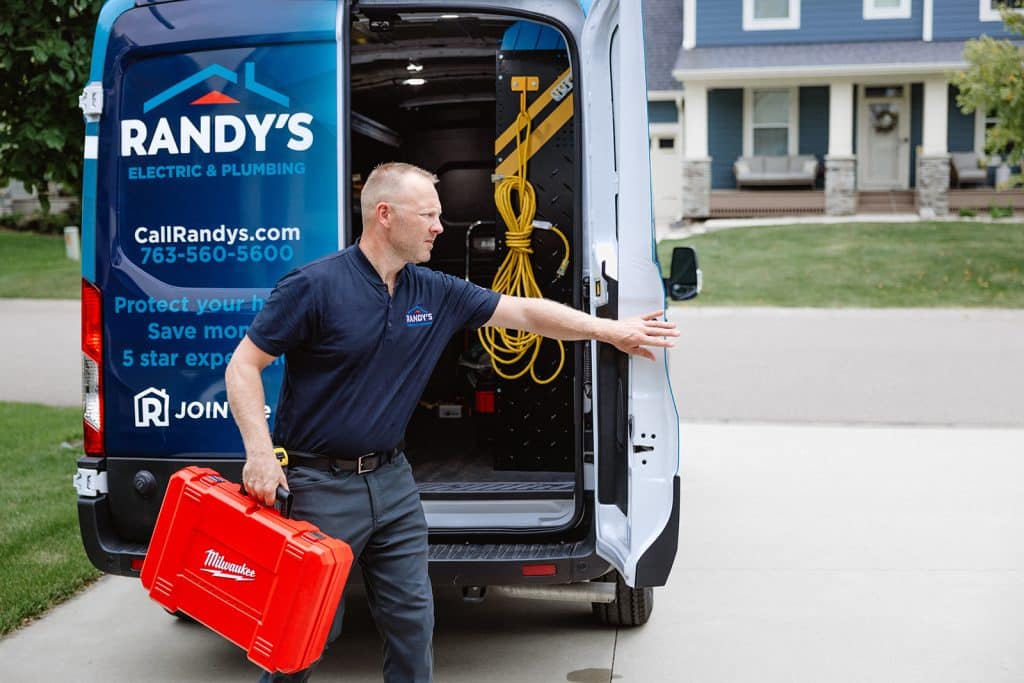 Service technician with red toolbox at Randy’s Electric & Plumbing van outside a home, closing door before service call.