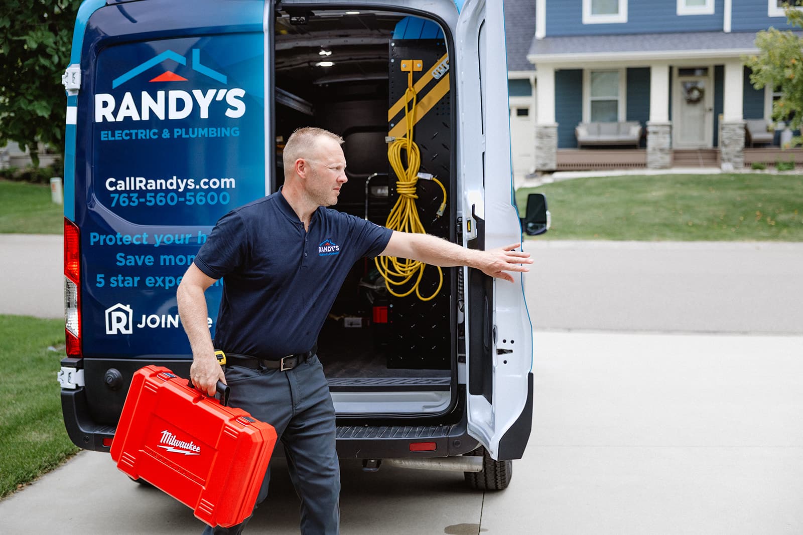 Service technician with red toolbox at Randy’s Electric & Plumbing van outside a home, closing door before service call.
