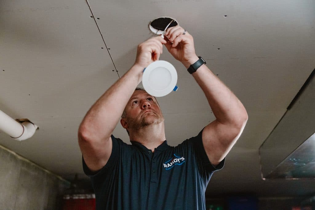 A electrician from Randy's installing a recessed LED ceiling light fixture in a basement ceiling