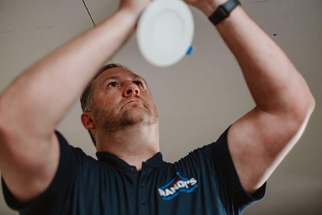 Electrician installing recessed LED ceiling light, close-up of handyman working indoors